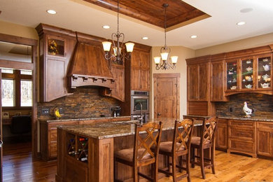 Inspiration for a large rustic u-shaped light wood floor eat-in kitchen remodel in Minneapolis with an undermount sink, recessed-panel cabinets, medium tone wood cabinets, granite countertops, brown backsplash, stone tile backsplash, stainless steel appliances and an island