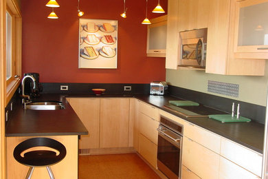 シアトルにあるモダンスタイルのおしゃれなキッチン (ダブルシンク、フラットパネル扉のキャビネット、淡色木目調キャビネット、黒いキッチンパネル、シルバーの調理設備) の写真