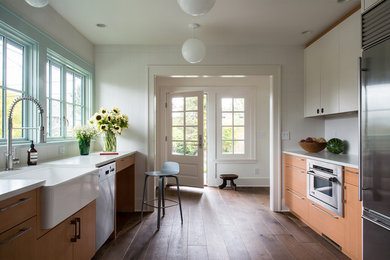 Inspiration for a mid-sized transitional u-shaped dark wood floor and brown floor enclosed kitchen remodel in Seattle with a farmhouse sink, flat-panel cabinets, medium tone wood cabinets, quartz countertops, white backsplash, ceramic backsplash, stainless steel appliances and no island