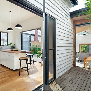 Mid-sized contemporary single-wall kitchen with flat-panel cabinets, white cabinets, stainless steel benchtops, white splashback, stainless steel appliances, medium hardwood floors, with island, brown floor and grey benchtop.