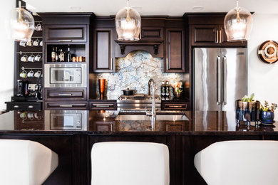 Mid-sized eclectic single-wall dark wood floor and brown floor open concept kitchen photo in Other with a double-bowl sink, raised-panel cabinets, dark wood cabinets, granite countertops, blue backsplash, glass sheet backsplash, stainless steel appliances, an island and brown countertops