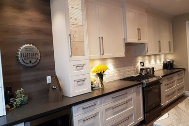 Example of a mid-sized transitional u-shaped medium tone wood floor and brown floor eat-in kitchen design in Toronto with an undermount sink, recessed-panel cabinets, white cabinets, marble countertops, white backsplash, brick backsplash, stainless steel appliances, an island and white countertops