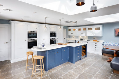 Design ideas for a large traditional l-shaped kitchen/diner in Other with a built-in sink, shaker cabinets, quartz worktops, white splashback, stainless steel appliances, limestone flooring, an island, brown floors, white worktops and white cabinets.