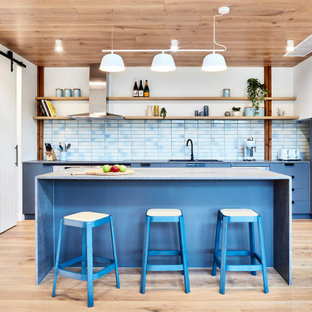 Mid-sized contemporary l-shaped eat-in kitchen in Melbourne with blue cabinets, ceramic splashback, light hardwood floors, with island, beige floor, a drop-in sink, flat-panel cabinets, blue splashback, stainless steel appliances, blue benchtop and wood.