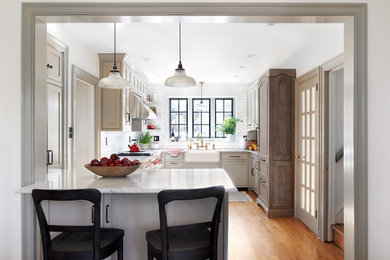 Example of a mid-sized transitional u-shaped medium tone wood floor and orange floor open concept kitchen design in Philadelphia with a farmhouse sink, beaded inset cabinets, beige cabinets, marble countertops, white backsplash, subway tile backsplash, paneled appliances, a peninsula and white countertops