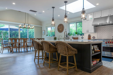 Eat-in kitchen - large craftsman single-wall porcelain tile, gray floor and vaulted ceiling eat-in kitchen idea in Los Angeles with an undermount sink, shaker cabinets, white cabinets, quartz countertops, white backsplash, subway tile backsplash, stainless steel appliances, an island and white countertops