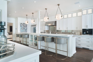 Example of a large beach style u-shaped dark wood floor and brown floor open concept kitchen design in Los Angeles with an undermount sink, recessed-panel cabinets, white cabinets, marble countertops, multicolored backsplash, glass sheet backsplash, stainless steel appliances, an island and white countertops