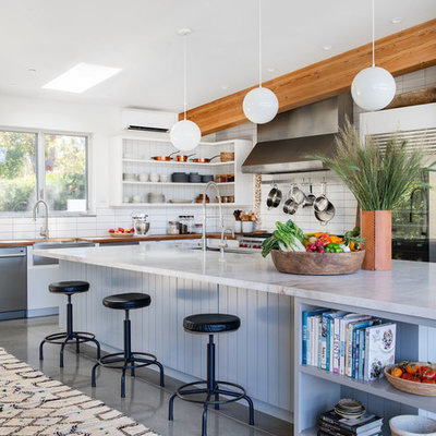 Trendy l-shaped gray floor and concrete floor eat-in kitchen photo in Los Angeles with a farmhouse sink, white backsplash, subway tile backsplash, stainless steel appliances, an island and white countertops