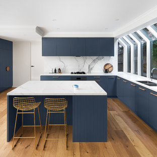 Design ideas for a large contemporary u-shaped open plan kitchen in Melbourne with blue cabinets, marble benchtops, white splashback, marble splashback, with island, a drop-in sink, flat-panel cabinets, stainless steel appliances, medium hardwood floors, brown floor and white benchtop.