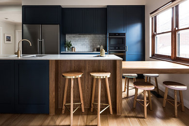 This is an example of a large traditional galley kitchen/diner in Melbourne with a submerged sink, shaker cabinets, blue cabinets, engineered stone countertops, grey splashback, marble splashback, stainless steel appliances, medium hardwood flooring, a breakfast bar and brown floors.