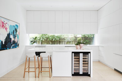 Design ideas for a large modern l-shaped open plan kitchen in Melbourne with a double-bowl sink, white cabinets, composite countertops, glass sheet splashback, stainless steel appliances, light hardwood flooring, an island, brown floors and white worktops.