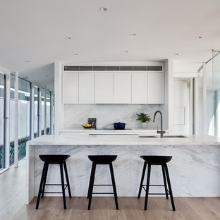Contemporary galley kitchen in Melbourne with an undermount sink, flat-panel cabinets, white cabinets, medium hardwood floors, with island, brown floor and white benchtop.