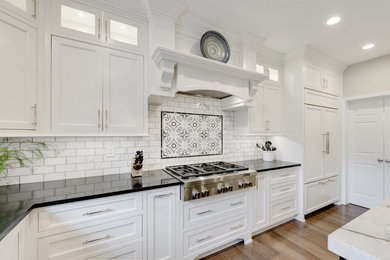 Example of a large transitional u-shaped medium tone wood floor and brown floor eat-in kitchen design in Philadelphia with recessed-panel cabinets, white cabinets, quartz countertops, white backsplash, subway tile backsplash, paneled appliances, an island and black countertops