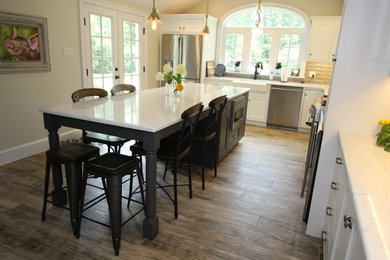 Inspiration for a large traditional l-shaped kitchen in Philadelphia with a belfast sink, flat-panel cabinets, white cabinets, engineered stone countertops, white splashback, ceramic splashback, stainless steel appliances, porcelain flooring, brown floors and white worktops.