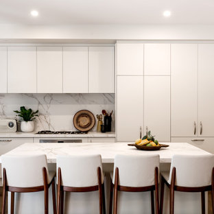This is an example of a mid-sized contemporary kitchen in Melbourne with an undermount sink, white cabinets, quartz benchtops, white splashback, stainless steel appliances, medium hardwood floors, with island, brown floor and white benchtop.