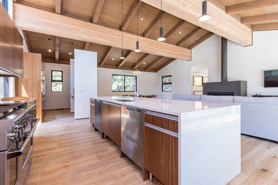 Inspiration for a large modern galley light wood floor open concept kitchen remodel in Los Angeles with an undermount sink, flat-panel cabinets, medium tone wood cabinets, solid surface countertops, white backsplash, stainless steel appliances, an island and stone slab backsplash