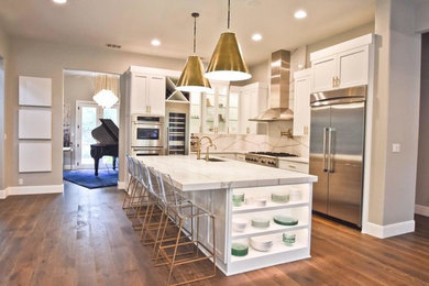 Inspiration for a mid-sized contemporary l-shaped medium tone wood floor and brown floor open concept kitchen remodel in Austin with an undermount sink, shaker cabinets, white cabinets, quartz countertops, white backsplash, stainless steel appliances, an island, white countertops and stone slab backsplash