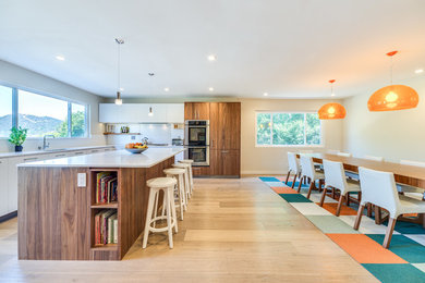 Foto de cocina vintage grande con armarios con paneles lisos, puertas de armario de madera oscura, electrodomésticos de acero inoxidable, suelo de madera clara, una isla, fregadero bajoencimera, encimera de acrílico, salpicadero blanco y suelo beige