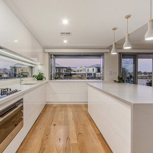 This is an example of a contemporary u-shaped eat-in kitchen in Perth with an undermount sink, flat-panel cabinets, white cabinets, window splashback, black appliances, medium hardwood floors, with island, beige floor and grey benchtop.
