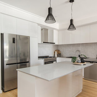 Inspiration for a mid-sized contemporary l-shaped kitchen in Perth with white cabinets, quartz benchtops, grey splashback, stainless steel appliances, laminate floors, with island, grey benchtop, flat-panel cabinets, a drop-in sink and beige floor.