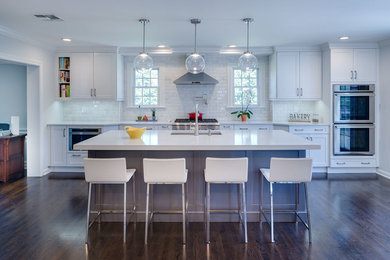 Example of a large transitional single-wall dark wood floor and brown floor eat-in kitchen design in New York with an undermount sink, recessed-panel cabinets, white cabinets, quartz countertops, white backsplash, ceramic backsplash, stainless steel appliances and an island