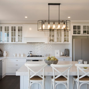 Design ideas for a transitional l-shaped eat-in kitchen in Other with a farmhouse sink, shaker cabinets, white cabinets, white splashback, stainless steel appliances, dark hardwood floors, with island, brown floor and white benchtop.