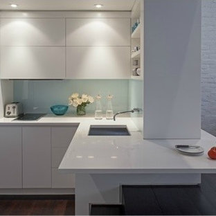 Small modern kitchen remodeling - Example of a small minimalist l-shaped dark wood floor kitchen design in New York with white cabinets, glass sheet backsplash, stainless steel appliances, an undermount sink, flat-panel cabinets, white backsplash and a peninsula