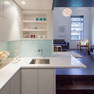 Foto de cocina en L, minimalista, pequeña, abierta, con fregadero bajoencimera, armarios con paneles lisos, puertas de armario blancas, salpicadero de vidrio templado, suelo de madera oscura, electrodomésticos de acero inoxidable, salpicadero blanco y península