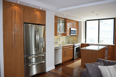 Photo of a small modern single-wall open plan kitchen in New York with stainless steel appliances, an island, a submerged sink, flat-panel cabinets, light wood cabinets, granite worktops, green splashback, glass tiled splashback and medium hardwood flooring.