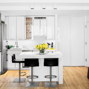 Small contemporary open concept kitchen pictures - Example of a small trendy l-shaped light wood floor and brown floor open concept kitchen design in New York with an undermount sink, flat-panel cabinets, white cabinets, marble countertops, white backsplash, stainless steel appliances and an island