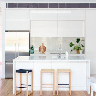 Design ideas for a mid-sized contemporary galley open plan kitchen in Sydney with an undermount sink, white cabinets, quartz benchtops, stainless steel appliances, light hardwood floors, with island, white benchtop, flat-panel cabinets, white splashback and brown floor.