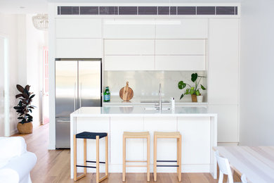 Foto på ett mellanstort funkis vit kök, med en undermonterad diskho, vita skåp, bänkskiva i kvarts, rostfria vitvaror, ljust trägolv, en köksö, släta luckor, vitt stänkskydd och brunt golv