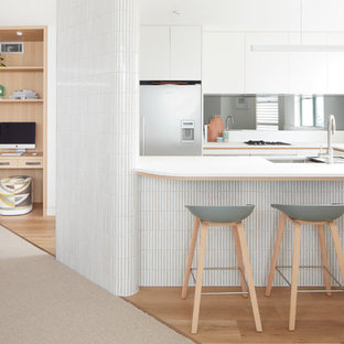 Mid-sized contemporary u-shaped kitchen in Sydney with a double-bowl sink, white cabinets, quartz benchtops, glass sheet splashback, stainless steel appliances, vinyl floors, no island, beige floor and white benchtop.