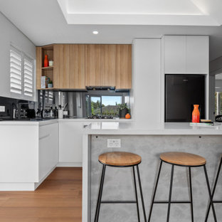 Mid-sized contemporary l-shaped open plan kitchen in Sydney with an undermount sink, flat-panel cabinets, white cabinets, quartz benchtops, metallic splashback, mirror splashback, stainless steel appliances, medium hardwood floors, with island, brown floor, white benchtop and vaulted.