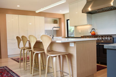 Exempel på ett stort modernt vit vitt kök och matrum, med en undermonterad diskho, släta luckor, skåp i ljust trä, bänkskiva i kvarts, vitt stänkskydd, stänkskydd i glaskakel, rostfria vitvaror, ljust trägolv, en köksö och beiget golv