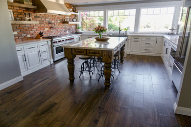 Large french country u-shaped medium tone wood floor and brown floor enclosed kitchen photo in Orange County with a farmhouse sink, raised-panel cabinets, white cabinets, marble countertops, red backsplash, brick backsplash, stainless steel appliances, an island and white countertops