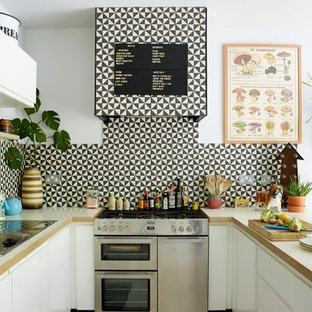 Medium sized bohemian u-shaped kitchen/diner in London with a double-bowl sink, flat-panel cabinets, white cabinets, wood worktops, white splashback, cement tile splashback, stainless steel appliances, painted wood flooring, a breakfast bar, white floors and white worktops.
