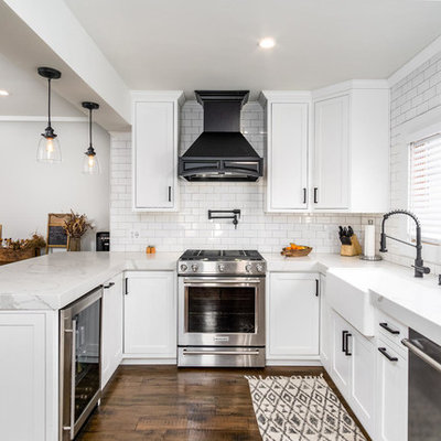 Elegant u-shaped dark wood floor and brown floor kitchen photo in San Diego with a farmhouse sink, shaker cabinets, white cabinets, white backsplash, subway tile backsplash, stainless steel appliances, a peninsula and white countertops