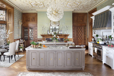 Example of a large ornate single-wall medium tone wood floor and brown floor enclosed kitchen design in New York with an undermount sink, recessed-panel cabinets, white cabinets, quartzite countertops, white backsplash, mosaic tile backsplash, paneled appliances and two islands