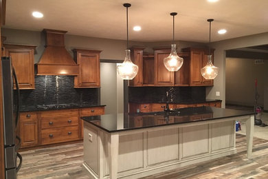 Example of a large transitional l-shaped porcelain tile eat-in kitchen design in Omaha with an undermount sink, raised-panel cabinets, medium tone wood cabinets, granite countertops, black backsplash, matchstick tile backsplash, stainless steel appliances and an island