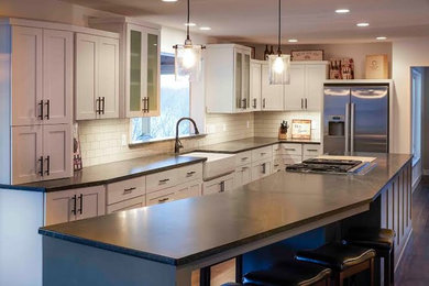 Photo of a contemporary kitchen/diner in Minneapolis with a belfast sink, shaker cabinets, white cabinets, soapstone worktops, white splashback, glass tiled splashback, stainless steel appliances, dark hardwood flooring and an island.