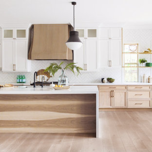 Esempio di una cucina classica con lavello sottopiano, ante con riquadro incassato, ante in legno chiaro, paraspruzzi bianco, elettrodomestici in acciaio inossidabile, pavimento in legno massello medio, isola, pavimento marrone e top bianco