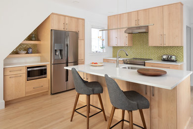 Contemporary kitchen in Boston with a submerged sink, flat-panel cabinets, light wood cabinets, green splashback, stainless steel appliances, light hardwood flooring, an island, beige floors and white worktops.