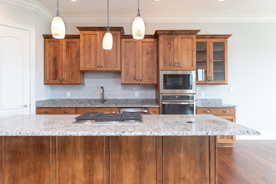 Open concept kitchen - mid-sized traditional l-shaped medium tone wood floor and brown floor open concept kitchen idea in Other with an integrated sink, flat-panel cabinets, brown cabinets, quartz countertops, gray backsplash, subway tile backsplash, stainless steel appliances, an island and multicolored countertops