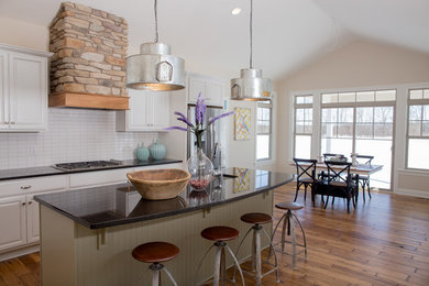 Mid-sized country dark wood floor and brown floor eat-in kitchen photo in Cleveland with a double-bowl sink, raised-panel cabinets, white cabinets, granite countertops, white backsplash, subway tile backsplash, stainless steel appliances and an island