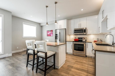 Eat-in kitchen - contemporary l-shaped medium tone wood floor eat-in kitchen idea in Vancouver with a double-bowl sink, flat-panel cabinets, white cabinets, solid surface countertops, white backsplash, subway tile backsplash, stainless steel appliances and an island