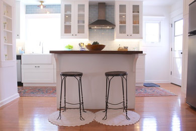 Large contemporary l-shaped enclosed kitchen in Los Angeles with a belfast sink, shaker cabinets, white cabinets, engineered stone countertops, blue splashback, metro tiled splashback, stainless steel appliances, medium hardwood flooring, an island and brown floors.