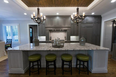 Inspiration for a large transitional medium tone wood floor kitchen remodel in Other with raised-panel cabinets, gray cabinets, granite countertops, gray backsplash, mosaic tile backsplash, stainless steel appliances and an island