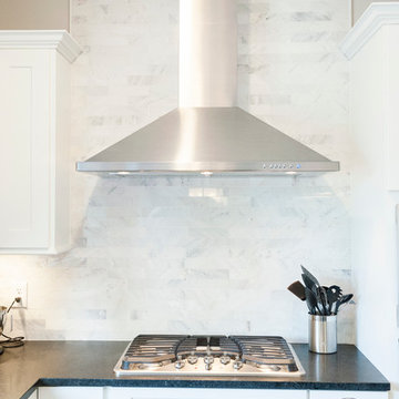 Marble subway tile backsplash and stainless steel hood in transitional kitchen
