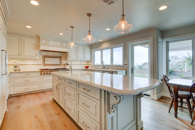 Inspiration for a large timeless u-shaped light wood floor open concept kitchen remodel in Orange County with an undermount sink, raised-panel cabinets, white cabinets, quartzite countertops, white backsplash, ceramic backsplash, an island and paneled appliances